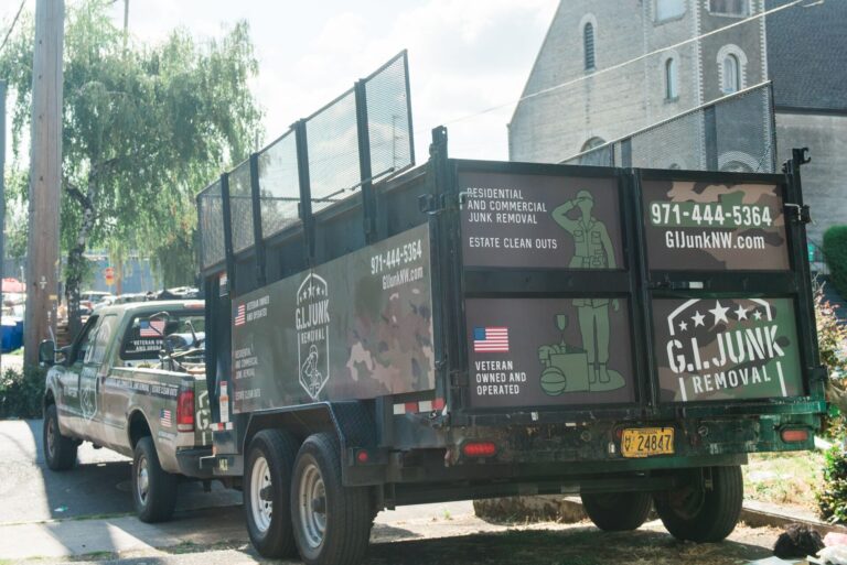 G.I. Junk Removal branded trailer and pickup truck parked on a street, showing camo-wrap graphics and contact info