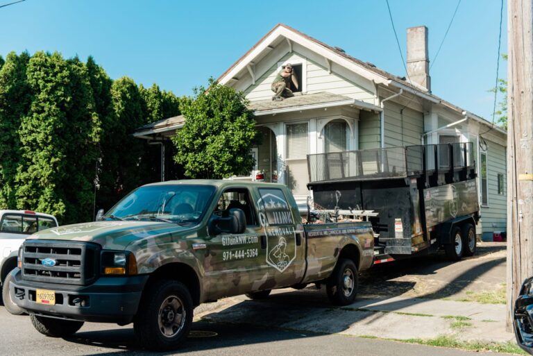 G.I. Junk Removal crew member in branded shirt rolling a blue bin toward the company truck in Oregon